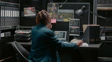 Police agent taking notes on case files in incident room, trying to solve criminal activity and catch suspect. Professional inspector examining research and surveillance photos. photo