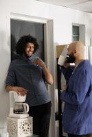 Two smiling arab businessmen having coffee break and talking in business office. Company employees standing with tea mugs while laughing and chatting in coworking space workplace photo
