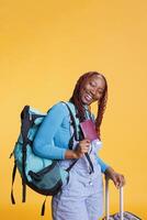 Smiling adult with passport on camera, feeling excited about international vacation destination. Cheerful woman preparing to board airplane, carrying luggage and identification pass. photo