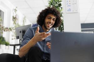 comienzo arriba empresa proyecto gerente teletrabajo, chateando con cliente en en línea reunión en ordenador portátil. joven árabe empleado que se discute producto lanzamiento con compañeros de trabajo en videollamada foto