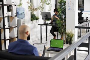 Executive analyzing reports, developing strategy and using laptop with green screen. Entrepreneur working at corporate portable computer with chroma key display in coworking space photo