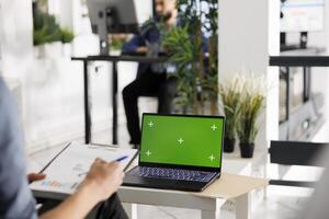 Financial analyst preparing for data analysis presentation using laptop with green screen in coworking space. Employee working at on portable computer with chroma key in business office photo