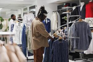 African american client looking at hanging shirts on rack in fashion boutique. Store customer checking apparel on hangers while choosing casual trendy outfit in shopping mall photo