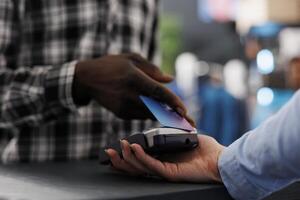 African american man shopper putting credit card on pos terminal paying formal for wear at counter desk in modern boutique, buying stylish clothes, fashionable accessories. Fashion concept. Close up photo