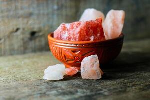 Himalayan pink salt rock in a bowl on a wooden background, selective focus photo