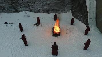 Gruppe von mit Kapuze durch das Feuer im das Berge. Filmaufnahme. das Szene von das Opfern im das Berge im Winter. religiös Ritual von Opfern von Zusatz video