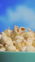 Vertical full HD footage of popcorns in turquoise bowl rotating against timelapse of clouds video