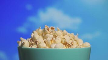 4K footage of popcorns in turquoise bowl rotating against timelapse of clouds video