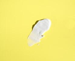 White smear of cosmetic cream on a yellow background. Creamy base texture isolated. A smear of face cream. Close-up of creamy texture photo