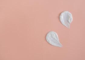 White smear of cosmetic cream on a beige background. Creamy foundation texture isolated. Smear of face cream. Close up of cream texture photo