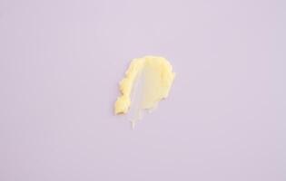 Cosmetic products creamy yellow stain texture on pink background. Texture of natural cosmetics, hair mask, cream, scrub photo