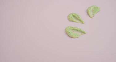 Sample of natural green scrub on a pink background. Peeling cream with microcapsules. Smear of apple or coffee scrub photo