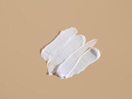 White smear of cosmetic cream on a beige background. Creamy foundation texture isolated. Smear of face cream. Close up of cream texture photo