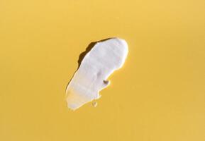 mancha blanca de crema cosmética sobre un fondo amarillo. textura base cremosa aislada. una mancha de crema facial. primer plano de textura cremosa foto