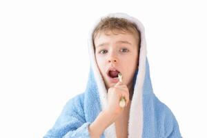 pequeño niño, chico en un azul terry túnica con un cepillo de dientes en blanco. un niño cepillos su dientes. cuidado de la salud y dental cuidado foto