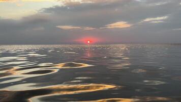 tranquilo puesta de sol terminado calma mar, con un vívido rojo Dom inmersión abajo el horizonte, reflejando en amable agua ondas, ideal para temas de natural belleza, paz, y verano tardes video