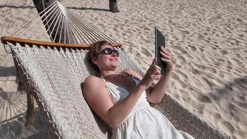 Digital Nomad Woman Relaxes with Tablet on Beach Hammock video