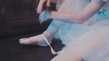 Unrecognizable girl ballerina dancer sits on floor on stage puts on pointe shoes ties satin ribbon around ankles prepares for ballet dance performance lesson, close-up of female legs. video