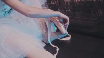 A ballerina puts pointe shoes on her feet while sitting on stage backstage before a performance. Professional ballet. The artist behind the scenes. video