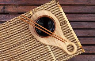 Bamboo mat, soy sauce, chopsticks on dark wooden table. Top view with copy space photo