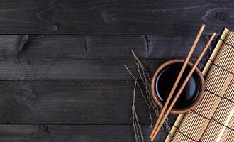 Bamboo mat, soy sauce, chopsticks on dark table photo