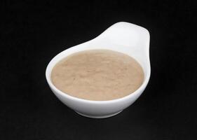 Peanut sauce. Tahini in white bowl isolated on black background photo