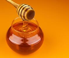 Honey stick and bowl of pouring honey isolated on yellow background photo