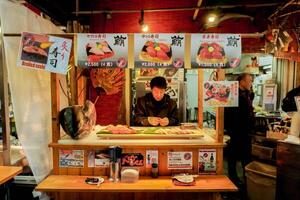 Osaka City, Japan 2023 -Japanese chef cooking fresh and raw sea foods for sale in his food booth at Kuromon street market, Osaka, Japan. photo