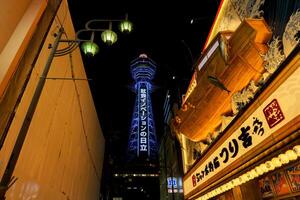 Osaka City, Japan, 2023- Perspective view of Japanese restaurant sign in wooden ancient Japanese fishing boat carving with Tsutenkaku tower One of Osaka's landmark on night time. photo