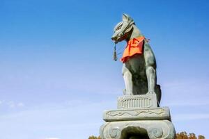 Kyoto City, Japan, 2023 - Fox statue of Fushimi Inari Shrine on blue sky background. In Japanese folk legend story that the fox represents the Inari god come to the human world give to exuberance. photo