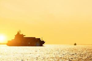 Silhouette of cargo ship with full shipload cargo containers are sailing in the Osaka bay evening with sun and lens flare background. photo