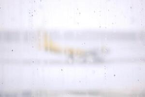 Raindrops on terminal airport's windows on blurry foggy and snowy outside with yellow plane on runway background. photo