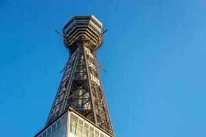 Osaka City, Japan, 2023 - Lookup view of Tsutenkaku tower on blue sky background. Tsutenkaku is a tower and one landmark of Osaka Total height is 103 m. Owned by Tstenkaku Kanko co. Ltd Co, Ltd. photo