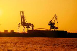 Silhouette of container crane at Osaka port are loading on evening with sunset color tone and gantry crane working background. photo