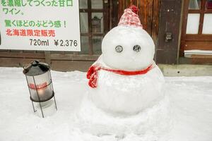 Sapporo City, Japan 2023 - Cute little snowman with vintage lantern on snow floor in winter season. Otaru city in winter was named city of love and destination of couples. photo