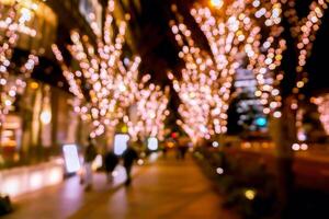 A beautiful blurred and bokeh of pink LED refection lighting decorate on trees in Valentines day with city night life in Osaka, Japan. photo