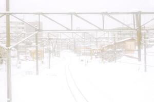 paisaje urbano ver y metal largo ferrocarril pista en invierno temporada y nieve tapado ciudad con completamente blanco brumoso desde nieve tormenta antecedentes. foto