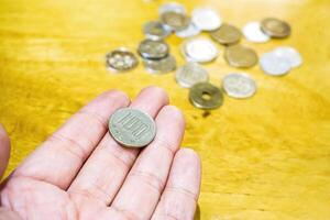 100 Yen Japanese coins on hand with blurry Japanese coins heap on wooden table background. photo