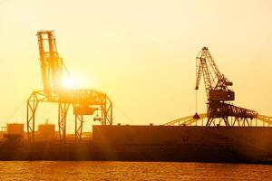 Silhouette of container crane at Osaka port are loading on evening with sunset color tone and gantry crane working background. photo