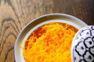 Closeup and crop Thai traditional sweet and dessert name's Foi Thong in Thai design white ceramic bowl on wooden table background. Foi Thong is considered as fine art dessert of Thai ancient. photo