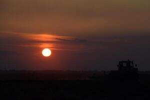 tractor arada arado el campo en un antecedentes puesta de sol. tractor silueta en puesta de sol antecedentes foto