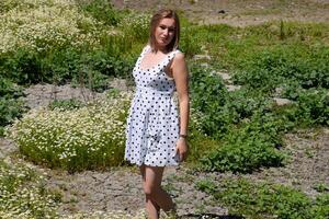 A woman in a white dress with polka dots is on a glade with daisies. Blooming daisies photo