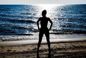 silueta de un hermosa niña figura en el antecedentes de el mar a puesta de sol foto