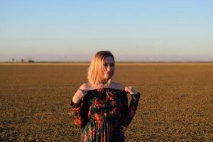 Woman in a plowed field in a red-black dress on a sunset background. photo