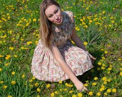 A girl in a dress in a clearing with dandelions. The girl among the flowers photo