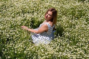 A woman in a white dress with polka dots is on a glade with daisies. Blooming daisies photo