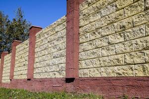 Fence made of bricks and decorative plaster. Yellow fence with red elements. High and beautiful fencing photo
