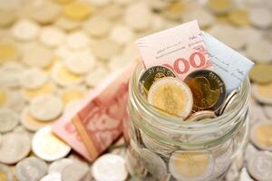 Close-up image of a glass jar full of new Thai baht banknotes and coins. Business and finance concept. photo