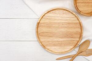 Empty round wooden plate with spoon and fork on white wooden table. Top view image. photo