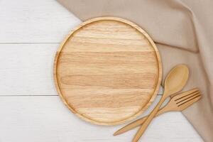 Empty round wooden plate with spoon and fork on white wooden table. Top view image. photo